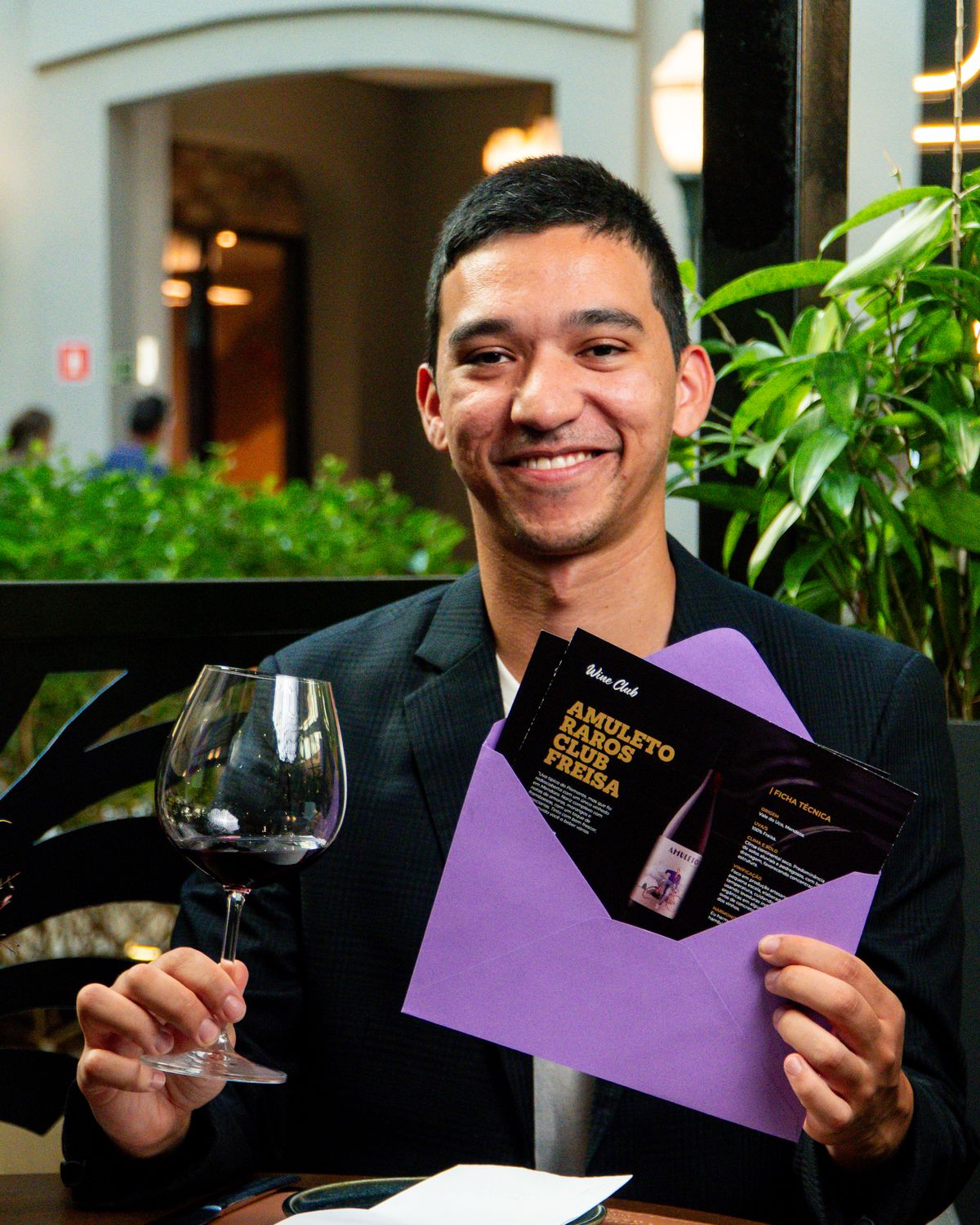 Sommelier do clube com uma taça e o envelope do mês nas mãos
